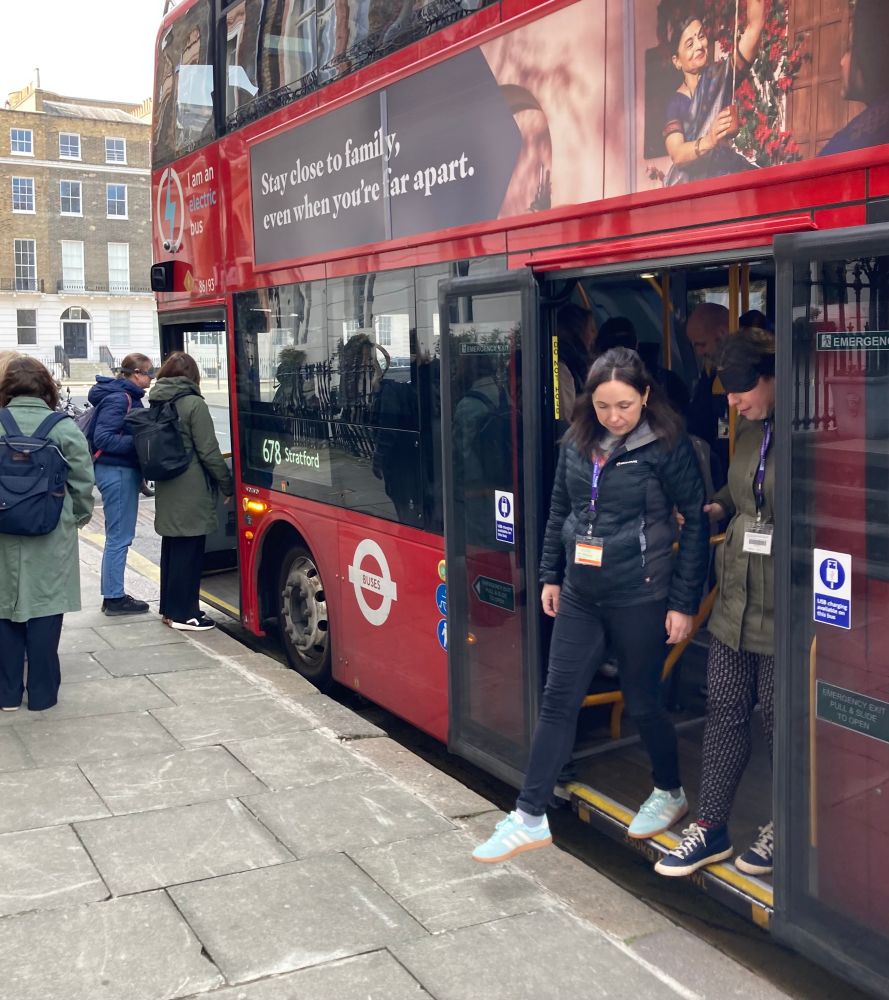 Habilitation students sight-guiding one another on and off a red, fully electric bus