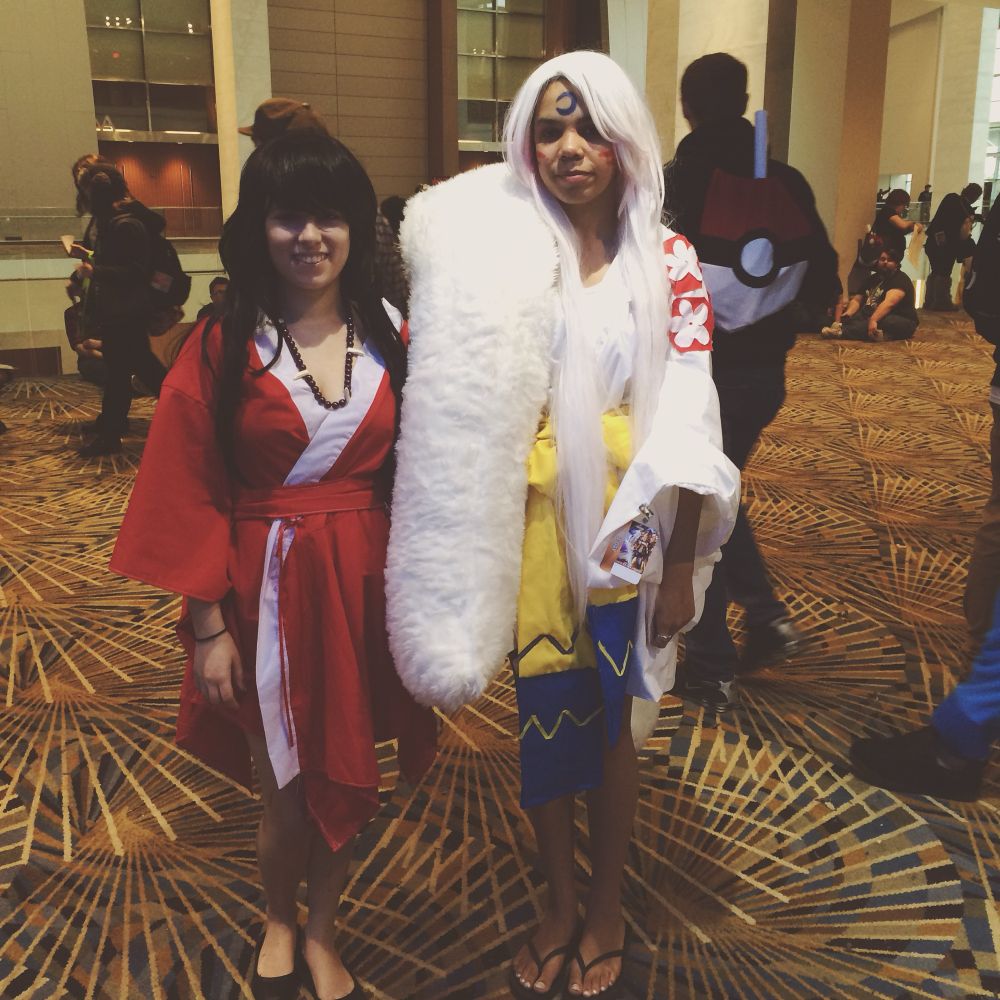 human form inuyasha wearing a red kimono and black hair stands on the left of white haired sesshomaru who is wearing a white, blue, yellow and red kimono with a large fluffy white shoulder piece. 