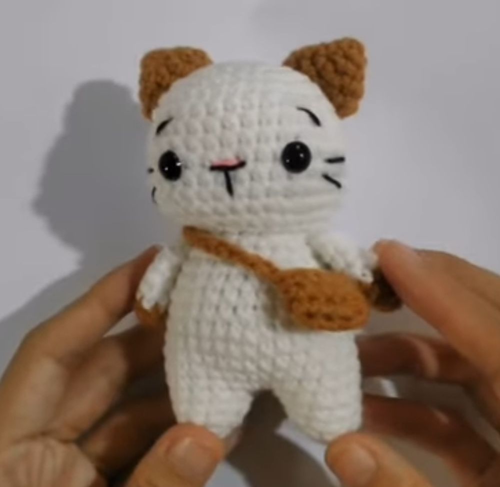 A brown and white crochet cat with beady little safety eyes and a little brown crochet bag to go with