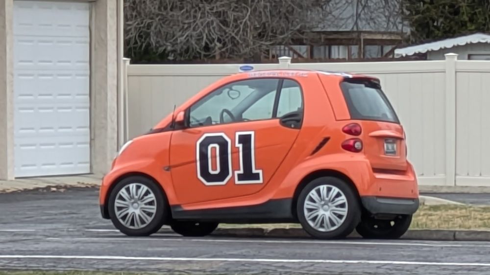 An obnoxiously orange Smart Car painted to resemble the General Lee, the famous muscle car from the Dukes of Hazzard.
