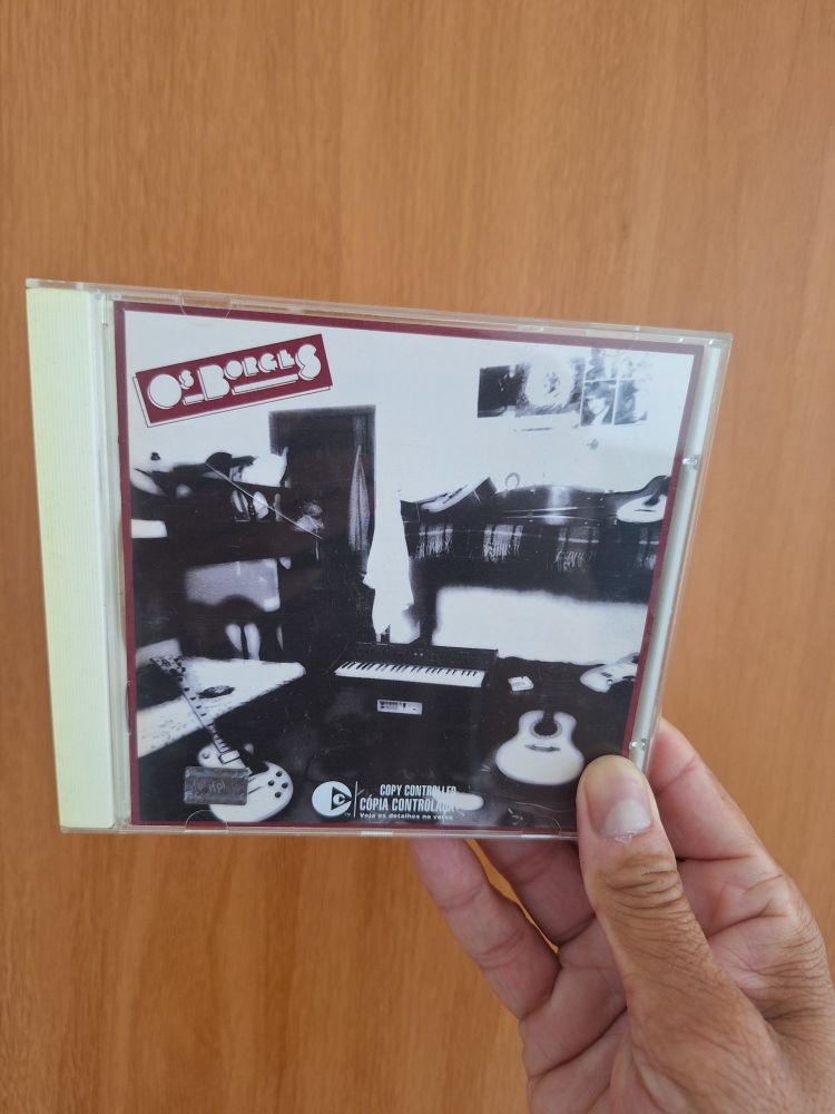 Minha mão segurando a capa do CD Os Borges. Ao fundo está a porta