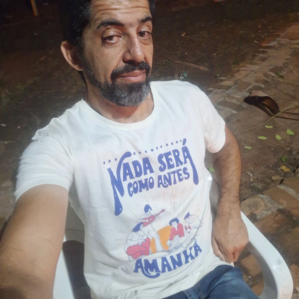 Selfie. Estou com cara de beudo, vestindo camiseta clara com a citação musical "Nada será como antes, amanhã "