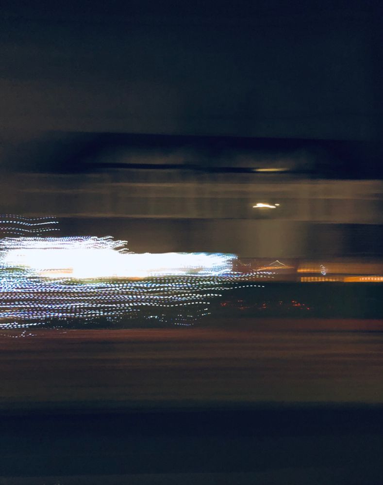 A blurred abstract photo taken from a moving car at night, passing a house with Christmas lights on an outdoor tree.