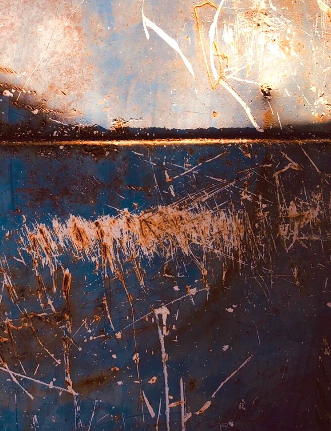Abstract detail of the side of a metal skip, badly scratched and rusting. The sunlight hits the top half aligning with a horizontal seam in the metal, the rest in shadow.
The gouges & scratches seem like drawn gestural marks & the horizontal seam & light give the impression of a landscape.