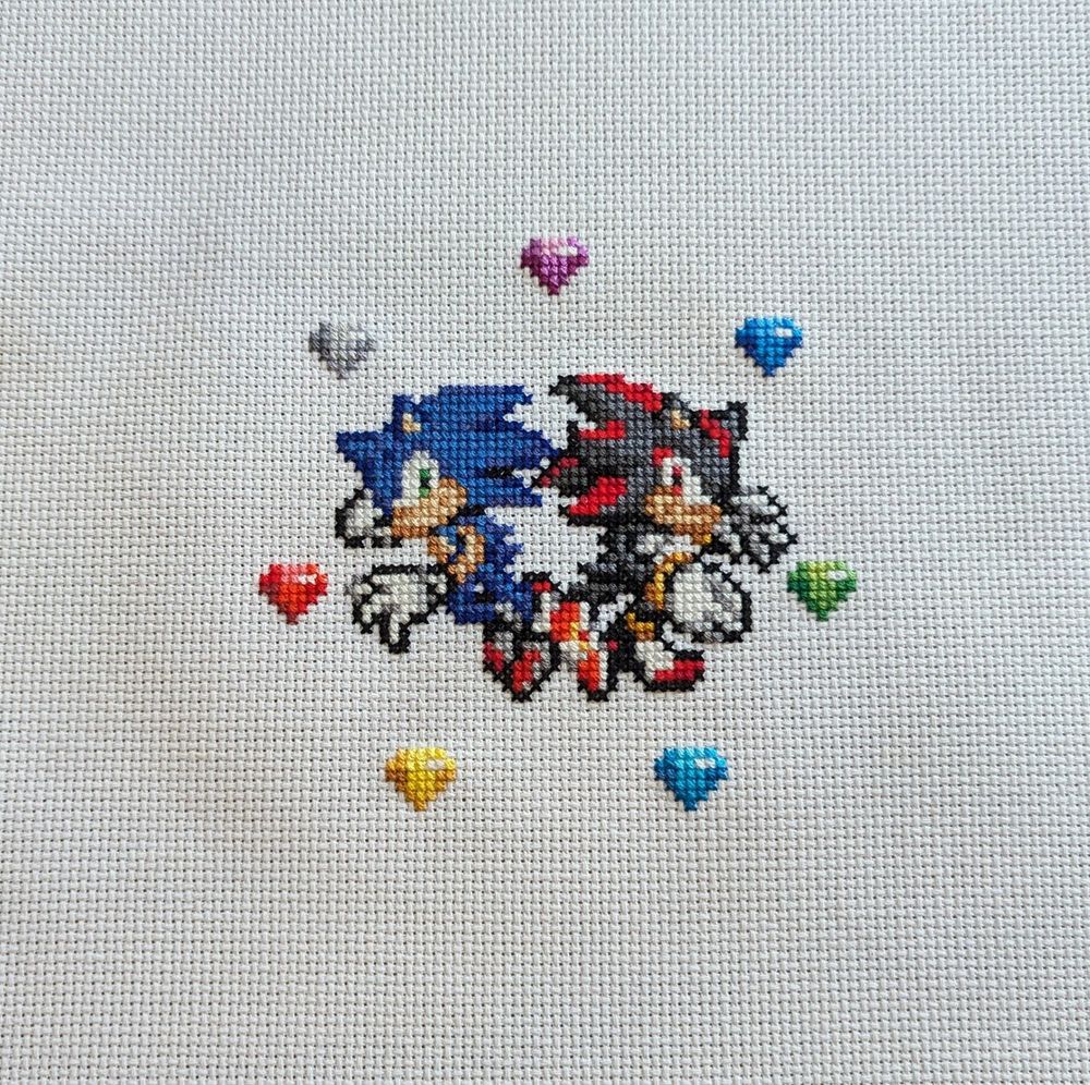 A cross stitch of the Sonic and Shadow pose from SA2 in pixel art form with 7 chaos emeralds surrounding them