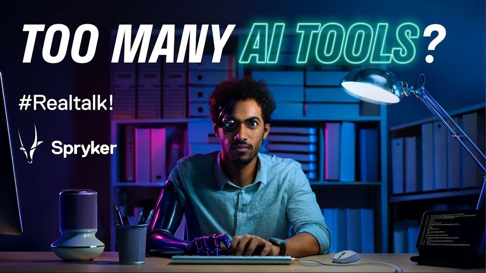 A software developer behind a desk with a keyboard, staring into the camera against a backdrop of a bookcase