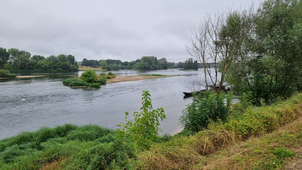 Loire river stream with a bridge in the distance, some wooden boots near the shore