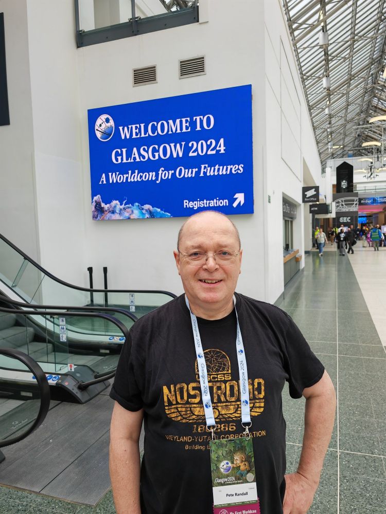 Me, grinning like an idiot in front of a sign reading "Welcome to Glasgow 2024, A Worldcon for Our Futures".