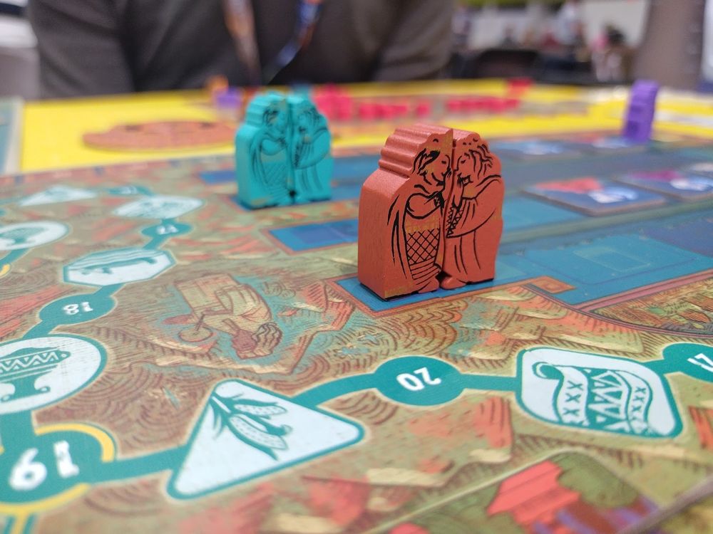 Wooden game pieces on a game board. They are a male and female figure nestled together, both in traditional Inca attire.