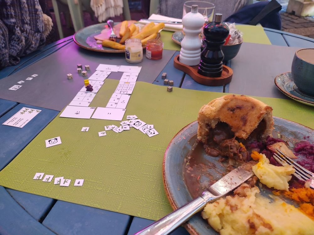 Half eaten meal in foreground, paper prototype of game with dice on table.