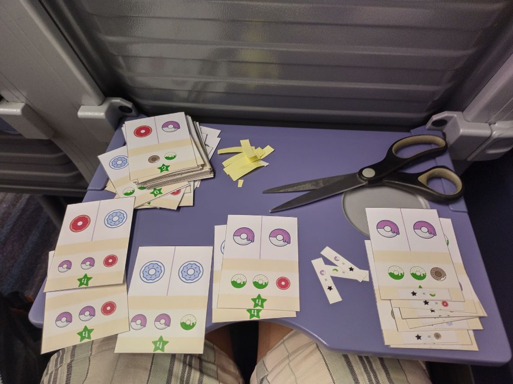 Cards showing doughnuts laid out on a train tray table with scissors. Stickers have been cut and added to some cards.
