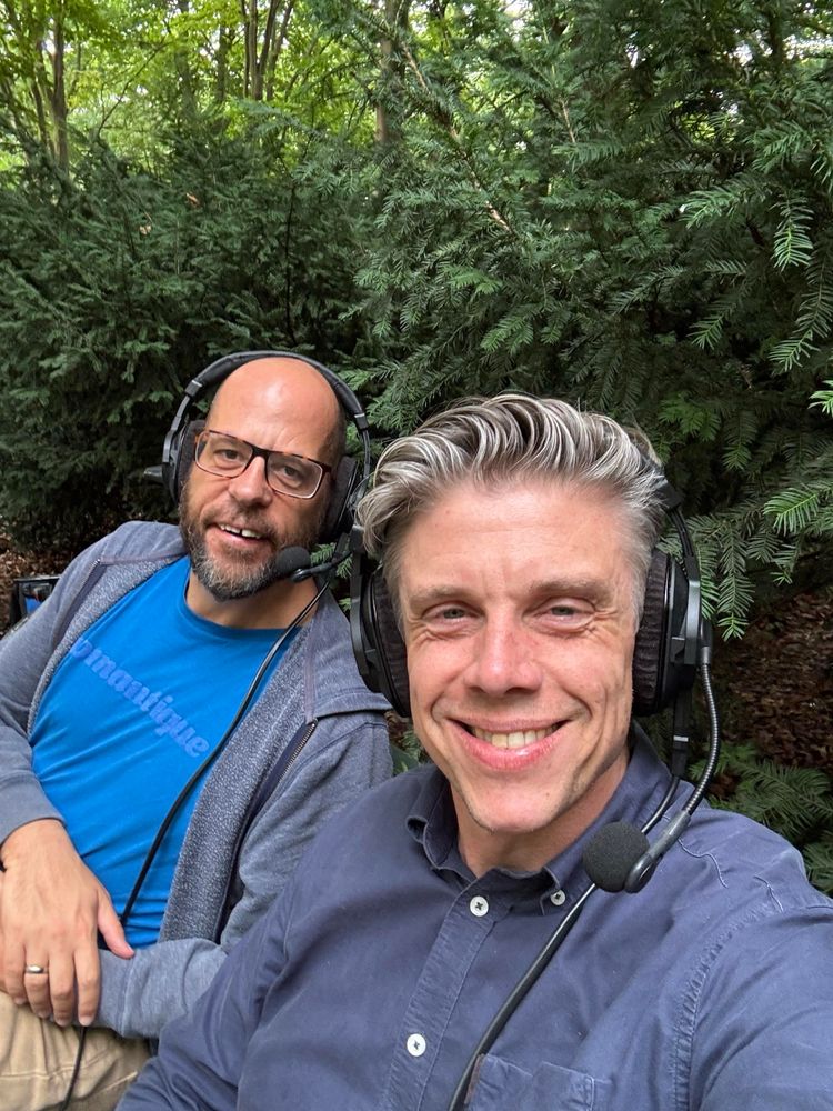 Markus und Christian auf einer Parkbank im Tiergarten, Podcast-Headsets auf dem Kopf