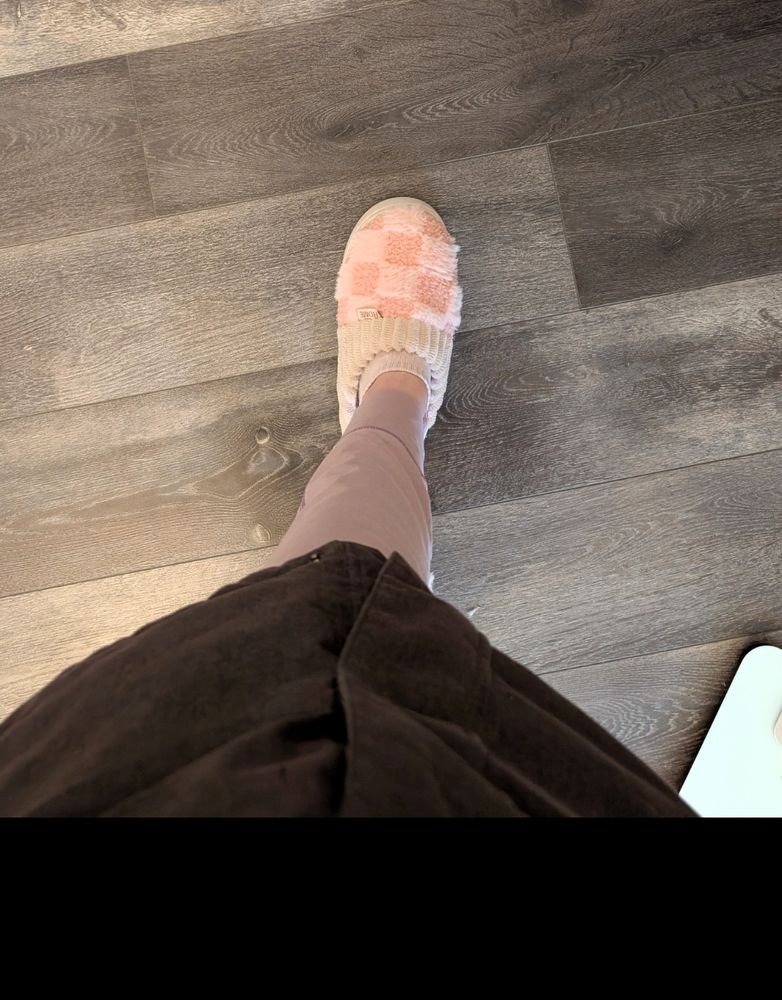 Top down photo showing the bottom of my winter coat, a calf with tights, naked ankle, and a fuzzy pink checkered slipper on the foot. 