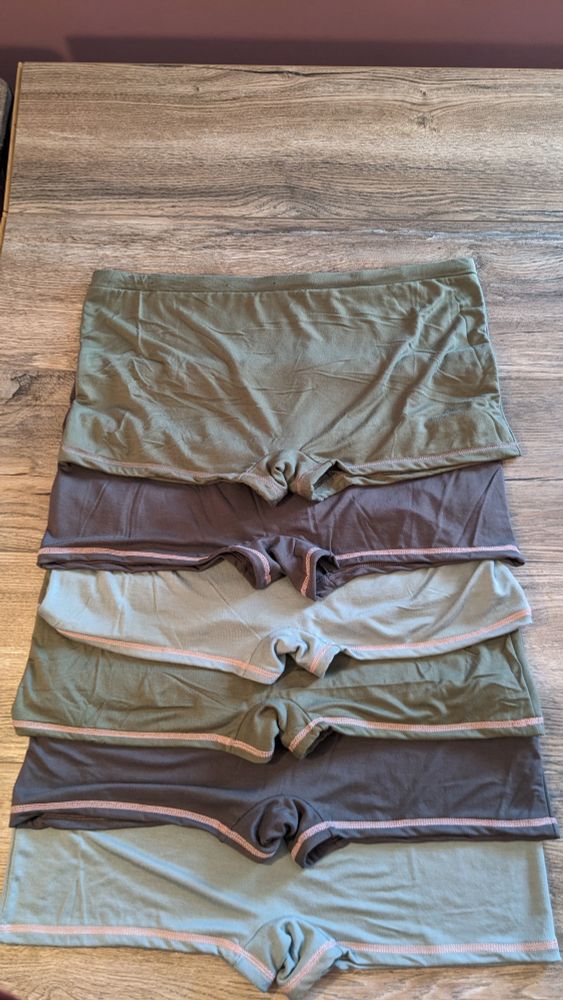 Six pairs of boyshorts style underwear in green, gray, and sage colors, with pink flatlock hems. 