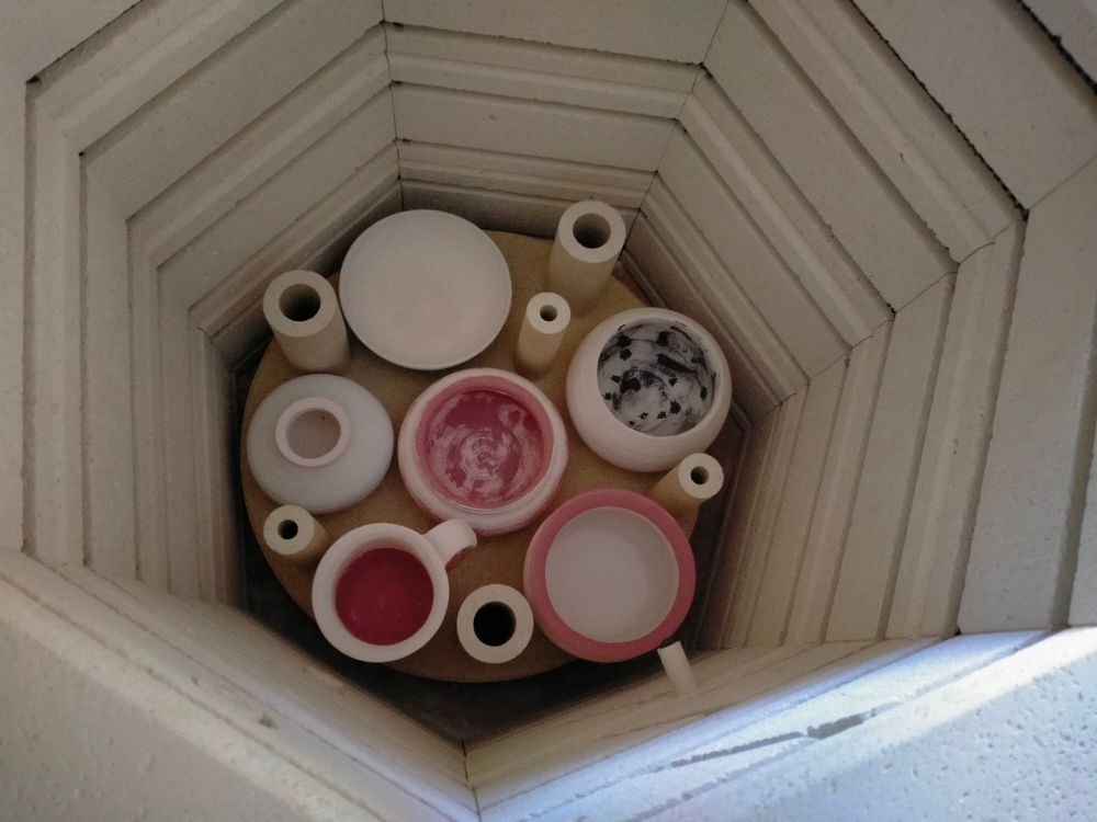 A shelf in a kiln loaded with pots for glaze firing and support struts