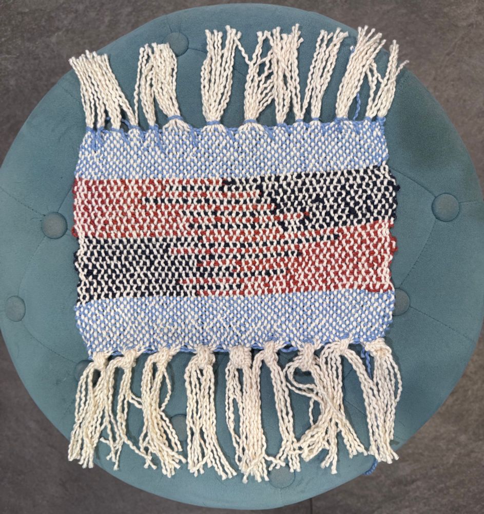 Small weaving sampler with cream warp. The ends are blue weft. The middle is a pattern of dark blue and copper in a random pattern