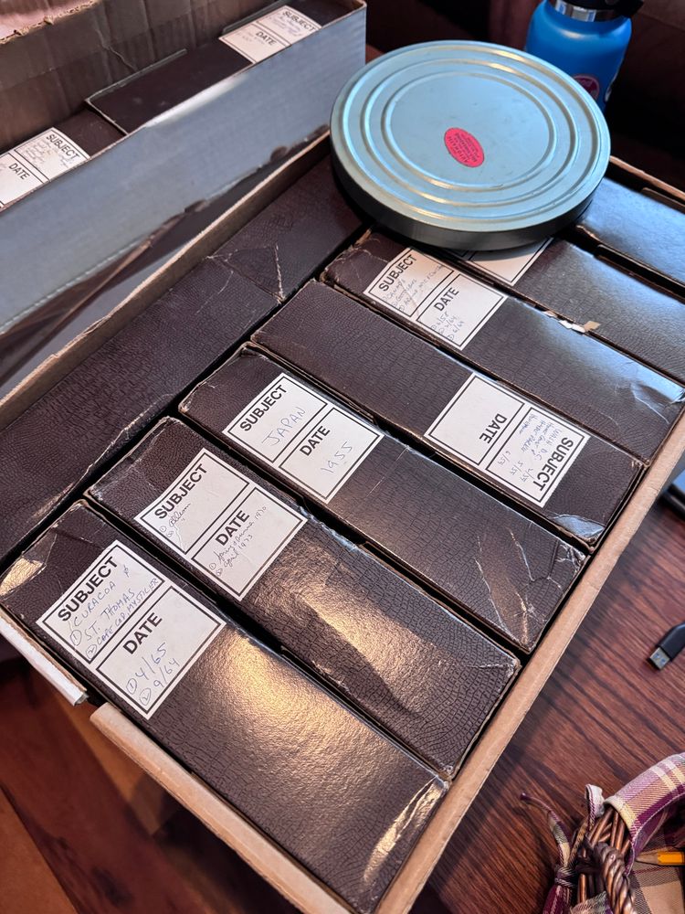 Boxes of labeled slide carousels in a box. An 8mm(?) canister home movie rests on top of the box 