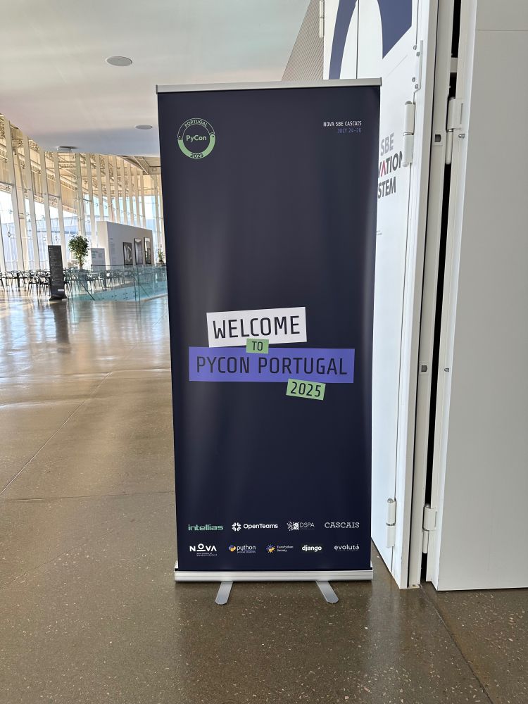 A picture in a large hall showing a PyCon Portugal banner that reads “Welcome to PyCon Portugal 2025”.