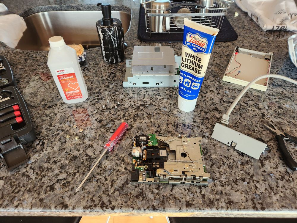 View of a disassembled 800k external Apple 3.5 inch floppy drive, with isopropyl alcohol and lithium grease visible behind it.