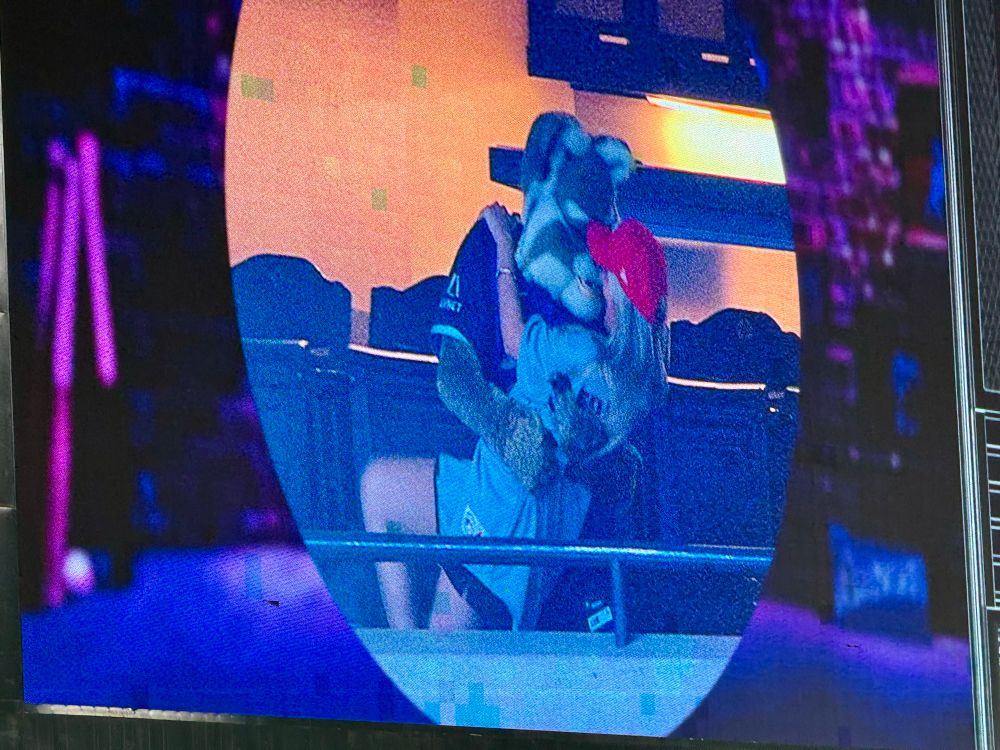 On the Kiss Cam, Arizona Diamondbacks mascot Baxter embraces and dips down a female St. Louis Cardinals fan with long blond hair who’s wearing a gray Cardinals jersey and a red ball cap.