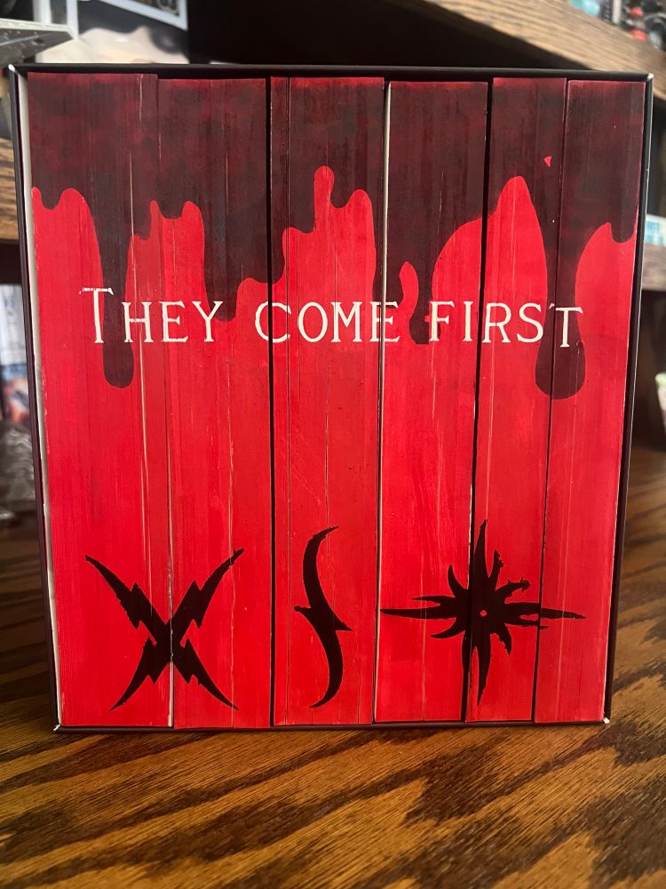 Red painted edges of Vampire Academy series with darker dripping blood over the Dhampir saying ‘They come first’ with Molnija, Zvezda, and Promise marks across the bottom. 