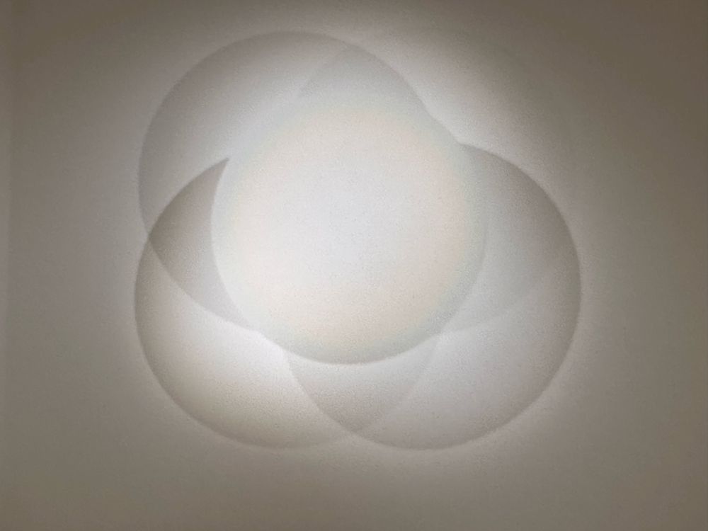 A white, circular, aluminum disk illuminated by several lights casting many shadows. An art piece by Robert Irwin at the Walker Art Center.