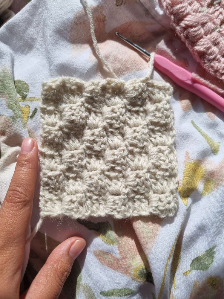 Picture of a small crochet corner to corner square in off white yarn with my hand in the picture for size reference