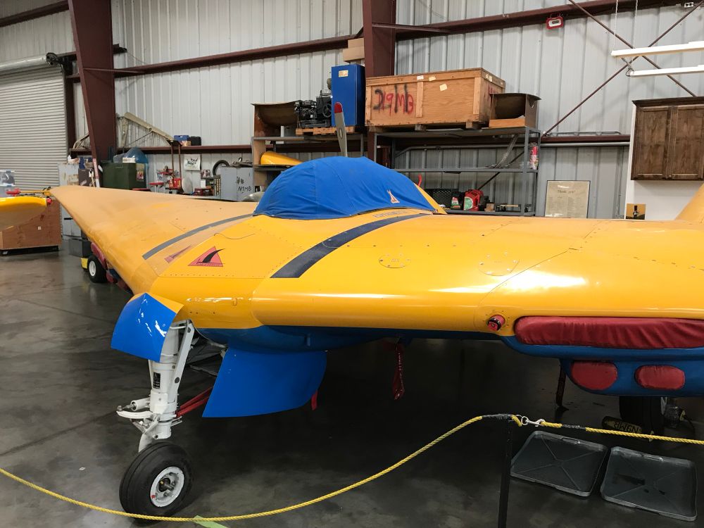 A yellow flying wing aircraft in a hangar workshop undergoing restoration taped up and cordoned off