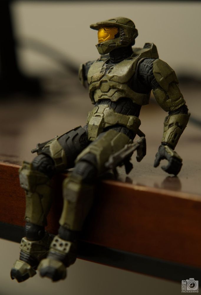 A Halo 2 Master Chief action figure sitting on a raised wooden platform. The posture is relaxed.