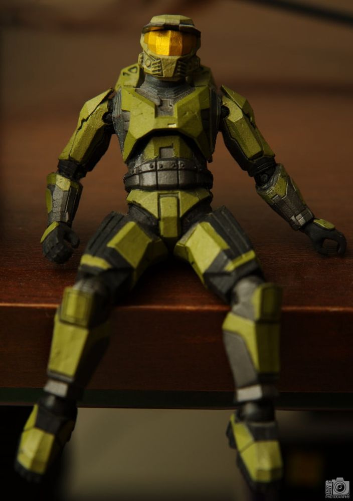 A Halo: Combat Evolved Master Chief action figure sitting on a raised wooden platform in a relaxed posture.