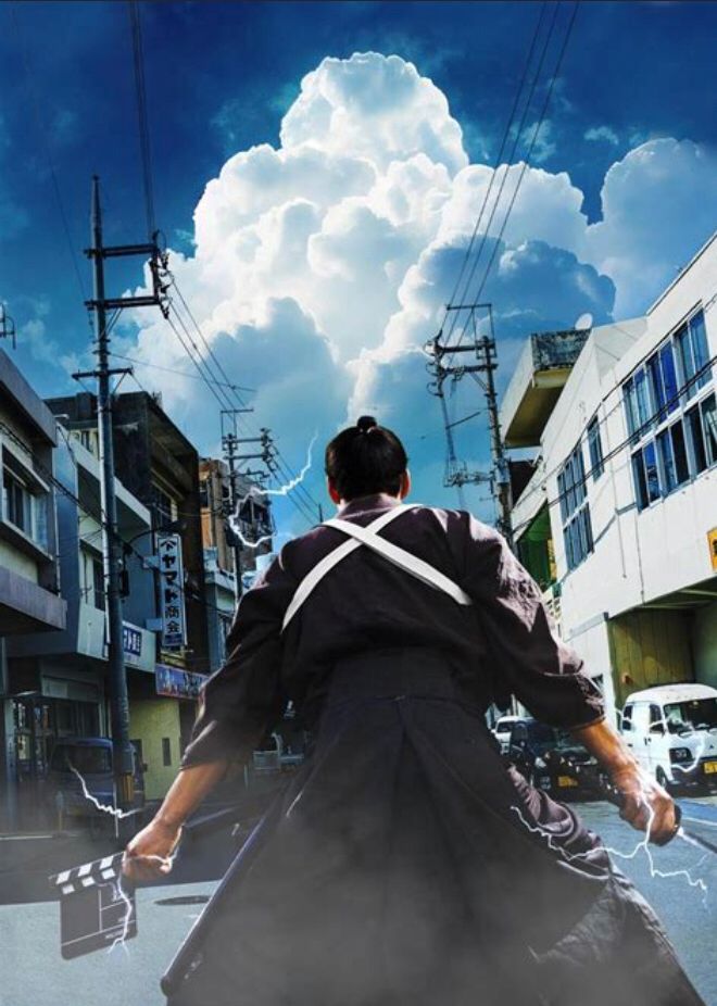 A samurai seen from behind, apparently ready to fight, a clapper in one hand and a sword in the other, surrounded by a modern world.