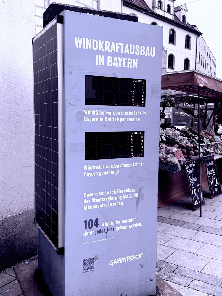 Das Bild zeigt eine Solarstrom betriebene Info Säule von Greenpeace im Zentrum von München. Darauf steht:
Windkraftausbau in Bayern
0 Windräder wurden dieses Jahr in Bayern in Betrieb genommen
0 Windräder wurden dieses Jahr in Bayern genehmigt

Bayern soll nach Beschluss der Staatsregierung bis 2040 klimaneutral werden.
104 Windräder müssten dafür jedes Kahr gebaut werden.