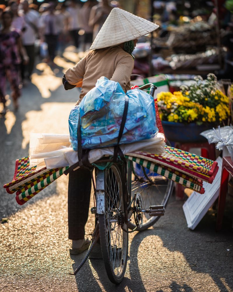 A woman walks her bike through the market in Hoi An, Vietnam during sunset. 