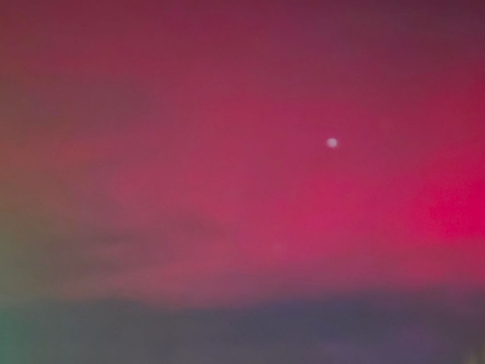 A zoom in of the sky over Casper, WY glowing an intense fuschia from the northern lights. A star or planet peeks through a little right of center. 