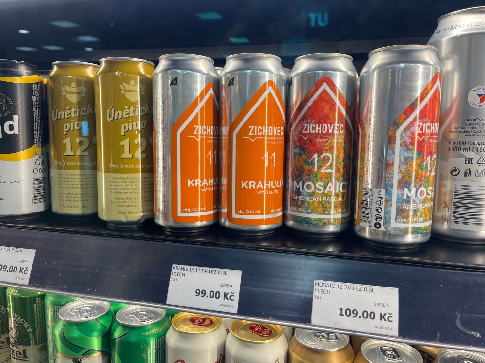 Cans of beer on a refrigerated store shelf. The two pale lagers cost 99 czk each, equal to about $4.75.