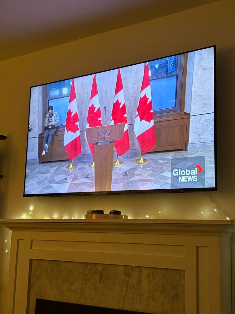 Man sitting down swinging his legs beside four Canadian flags while waiting for Prime Minister Justin Trudeau to speak