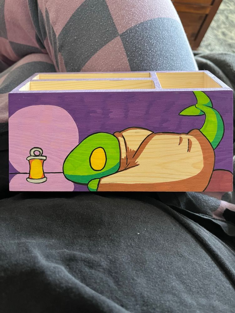 A wooded supplies holder with a tonberry from Final Fantasy laying down on the ground staring at a lantern.
