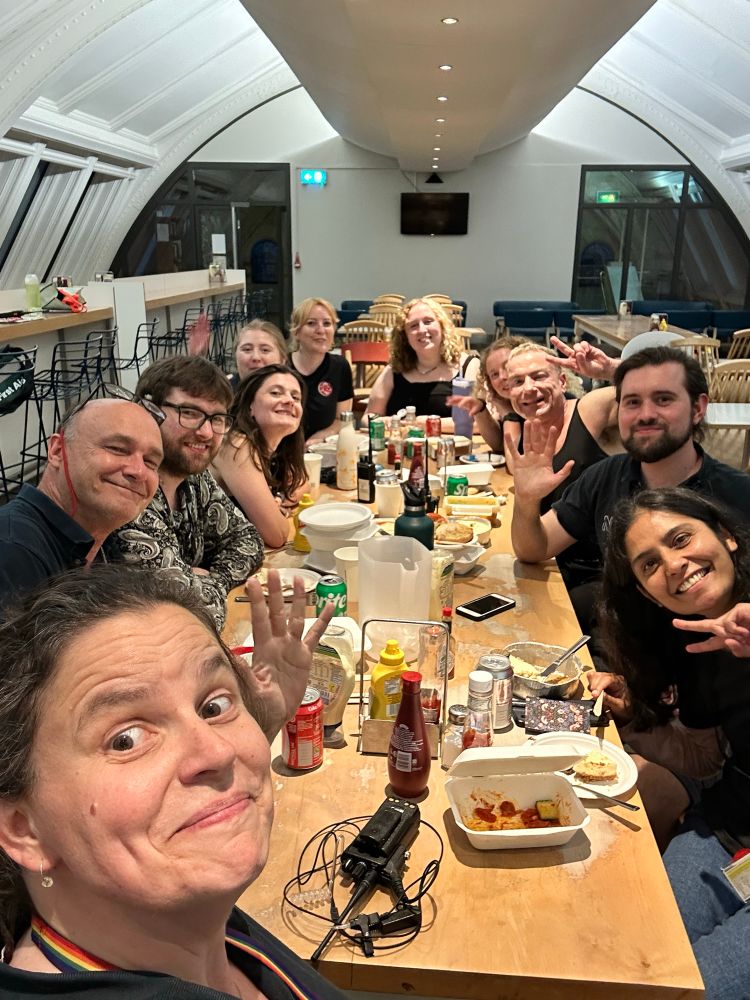 A group of eleven people sitting round an oblong table, eating a meal and smiling at the camera.