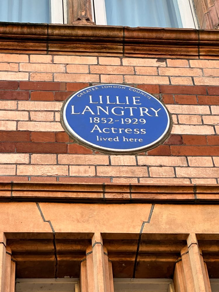 A blue historical plaque high up on a terracotta building. Reads ‘Lillie Langtry 1852-1929 actress love here.’