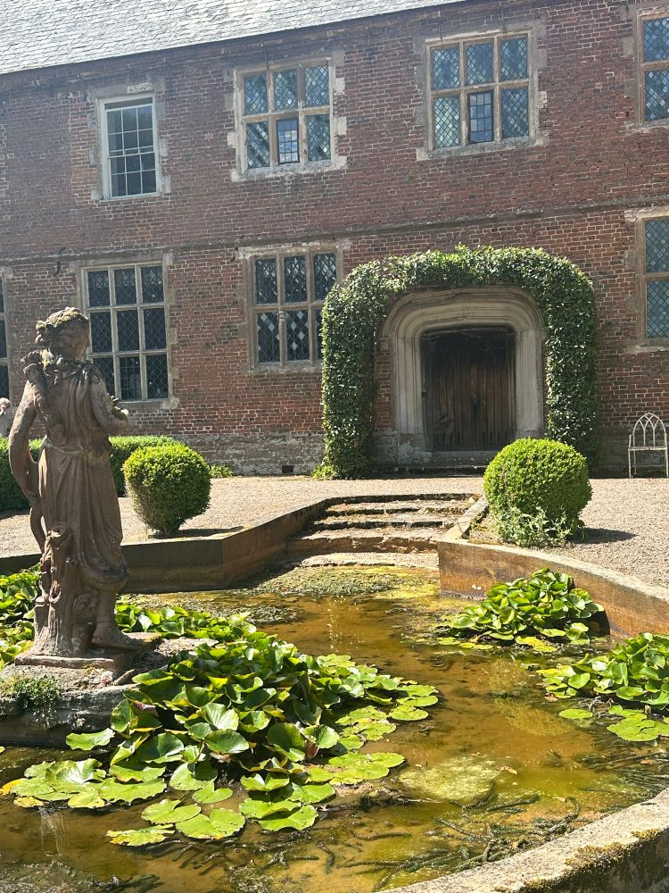 Decorative pond with statue of a woman, in front of a Manor House.