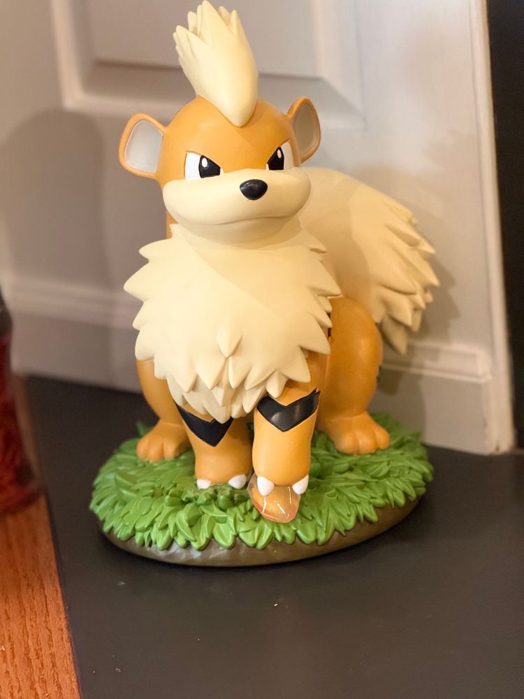 Photo of a Growlithe statue; its left paw is on top of a fire store and sitting on top of grass. 