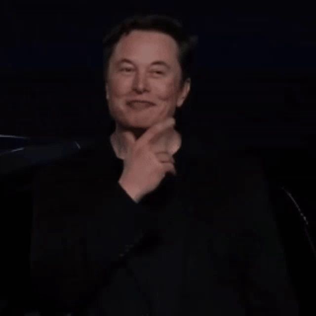 elon musk is smiling with his eyes closed in a dark room while wearing a black shirt .