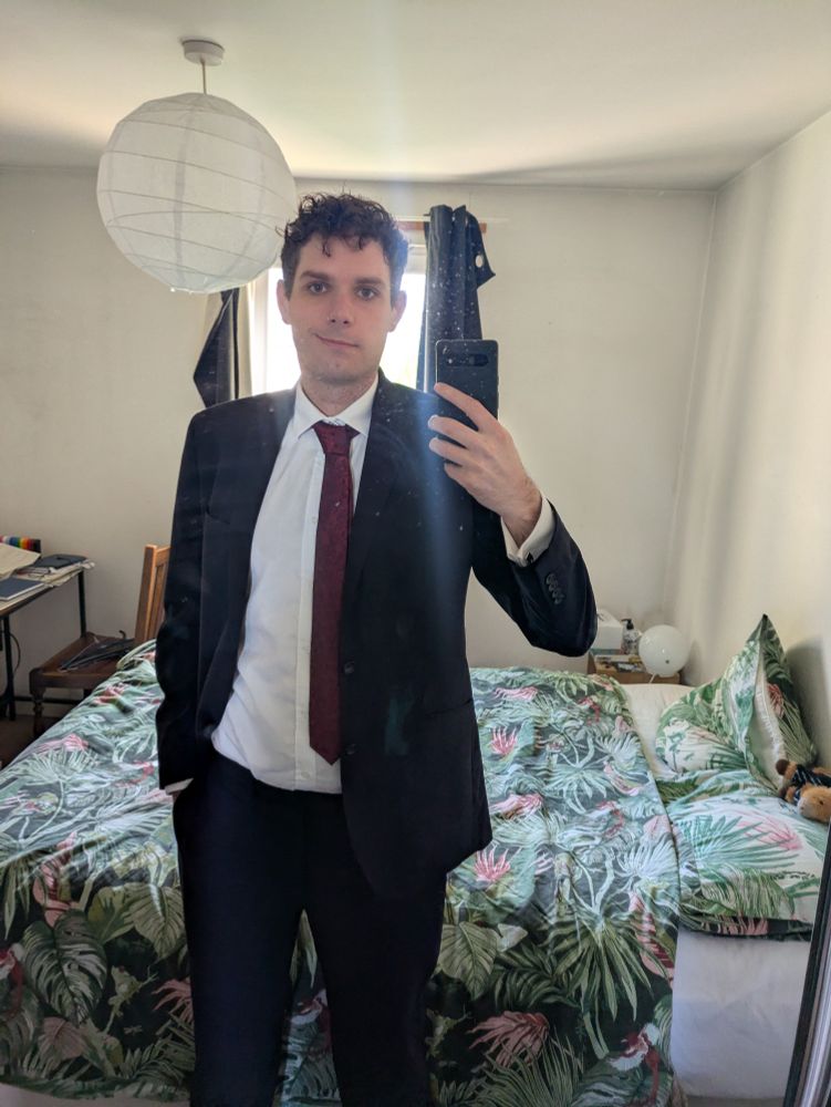 A mirror selfie in a suit. A tropical bedspread can be seen behind Alex.