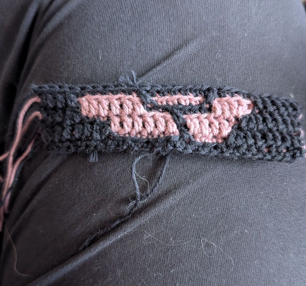 Seven rows of a mosaic crochet piece made with black and dusty pink yarn. It doesn't look like anything now, but it will eventually be a rectangular coaster that looks like a dusty pink rose on a black background.