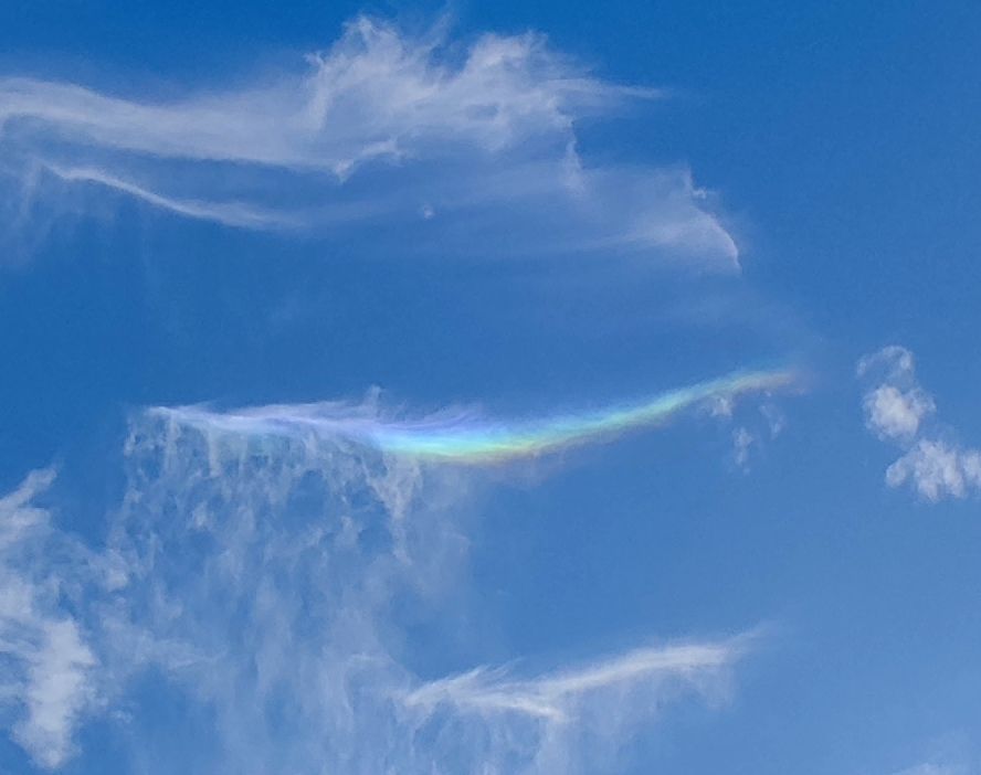 Blue sky with wispy white clouds one which has rainbow colours 