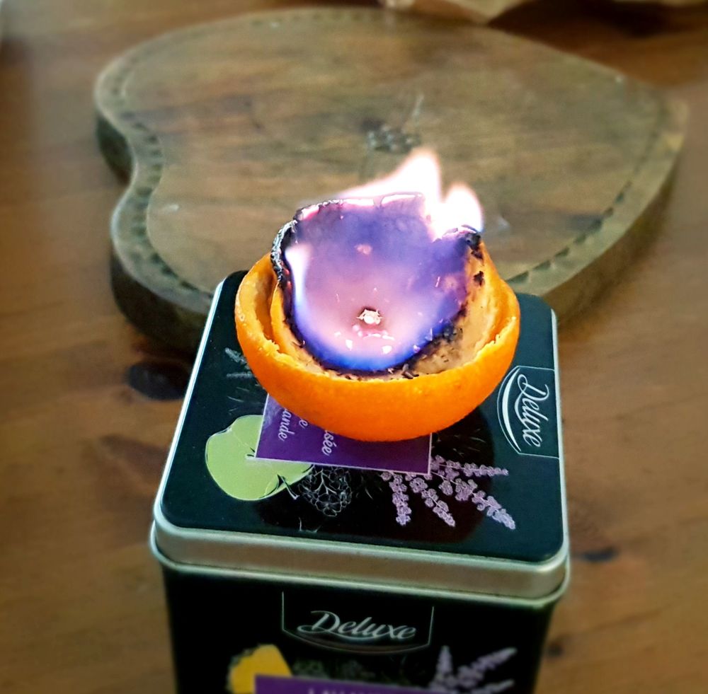 Sur une table en bois, gros plan sur la flamme bleue d'une peau de mandarine transformée en bougie