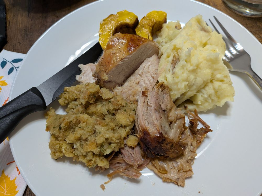 A plate of stuffing, roast turkey, slow roasted shredded pork, roasted squash, and mashed potatoes. A perfect combination of food for the thanksgiving holiday.