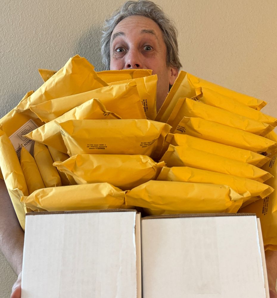OpenCase founder JOhn Rokos holding a pile of packages to ship after a flurry of orders that happened due to advertising on John Gruber's (of Daring Fireball) The Talk Show podcast.