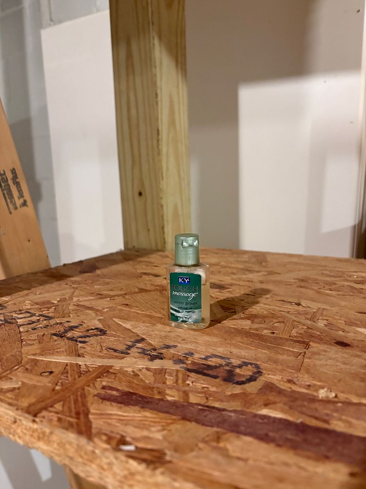 A small bottle of KY massage lubricant (‘Secret Forest’ scent) on a plywood shelf in a basement.  