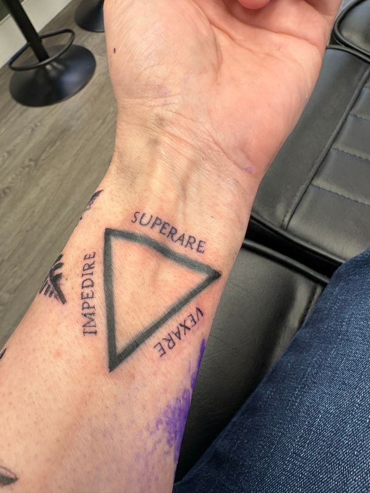 An image of a freshly-tattooed triangle with the Latin words Impedire - Vexare - Superare  (to hinder, to vex, to overcome) around it